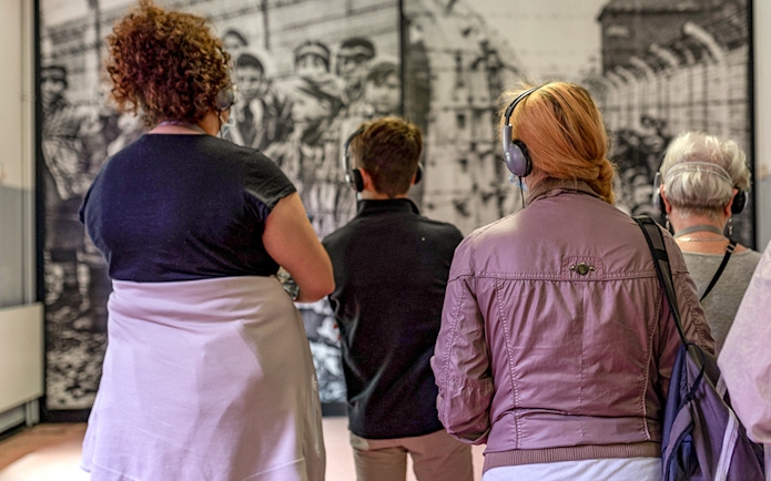 Visitors with headphones viewing Auschwitz exhibit during guided tour.