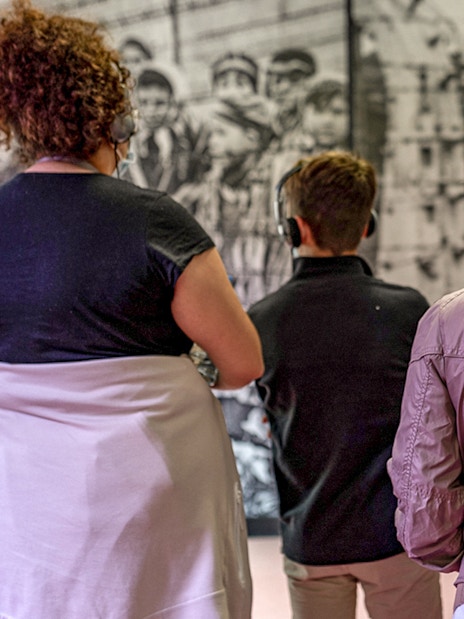 Visitors with headphones viewing Auschwitz exhibit during guided tour.