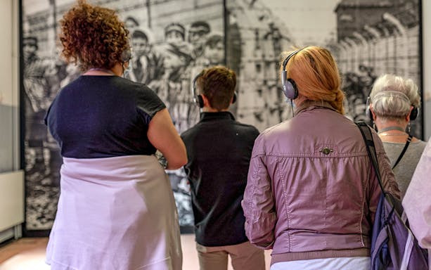 Visitors with headphones viewing Auschwitz exhibit during guided tour.