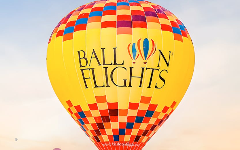Hot air balloon flying over desert landscape with passengers.