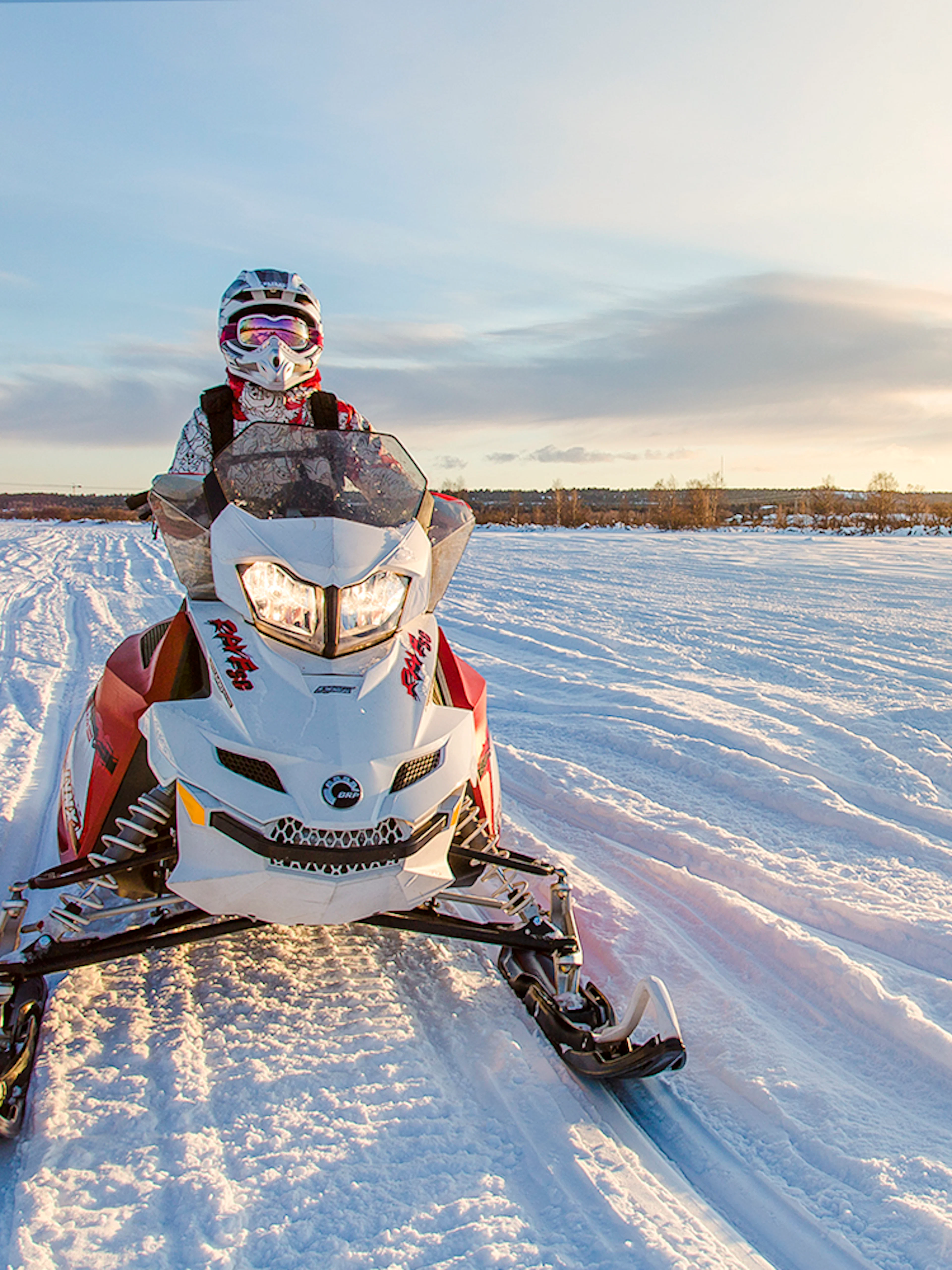 Snowmobile rider on snowy trail in Rovaniemi during sunset.