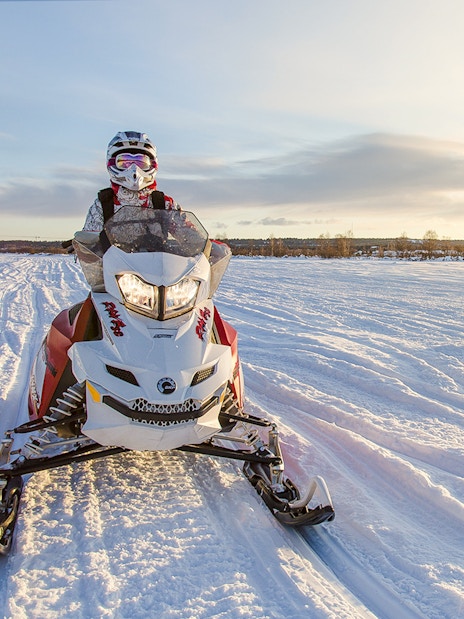 Snowmobile rider on snowy trail in Rovaniemi during sunset.