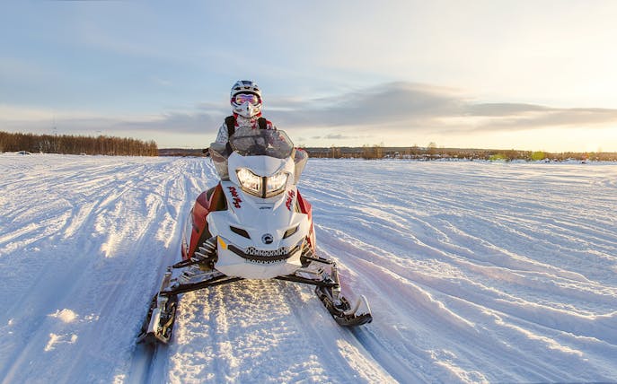 Snowmobile rider on snowy trail in Rovaniemi during sunset.