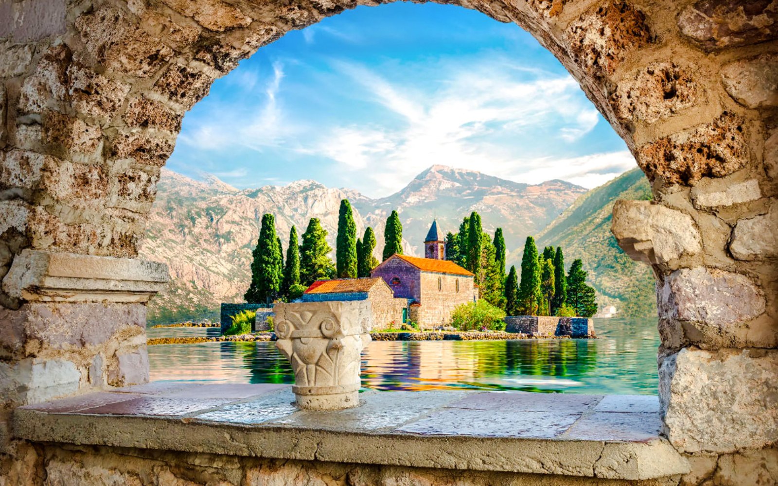 Our Lady of the Rocks island with church, framed by stone arch, Kotor Bay, Montenegro.