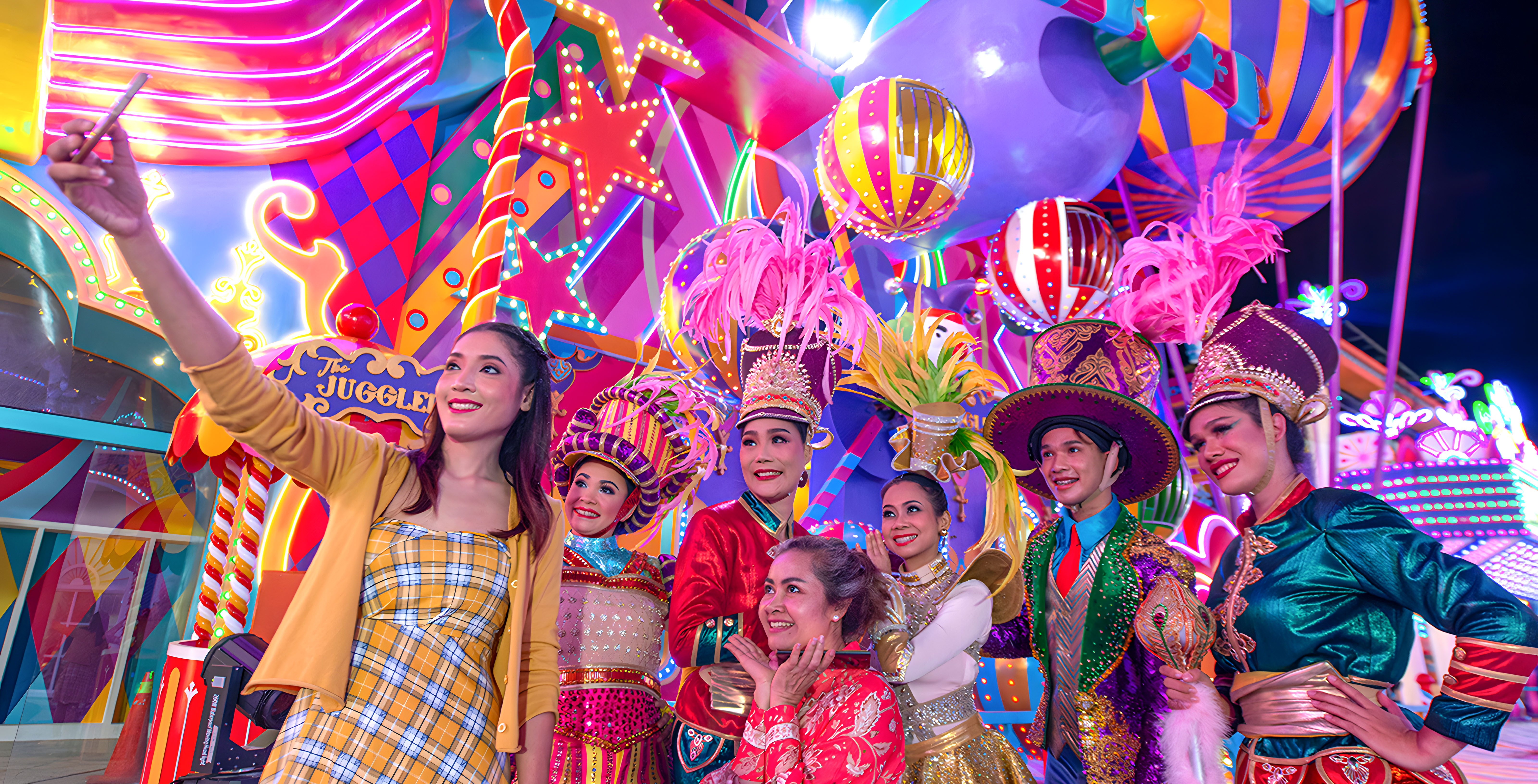Selfie de grupo en el Carnival Magic Phuket con las vibrantes carrozas del desfile de fondo.