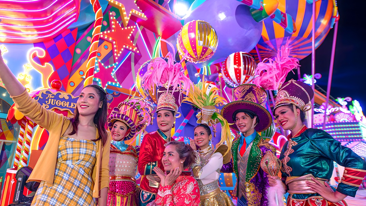 Gruppen-Selfie bei den Carnival Magic Phuket mit den farbenfrohen Wagen der Parade im Hintergrund.