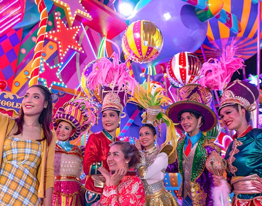 Group selfie at Carnival Magic Phuket with vibrant parade floats in the background.