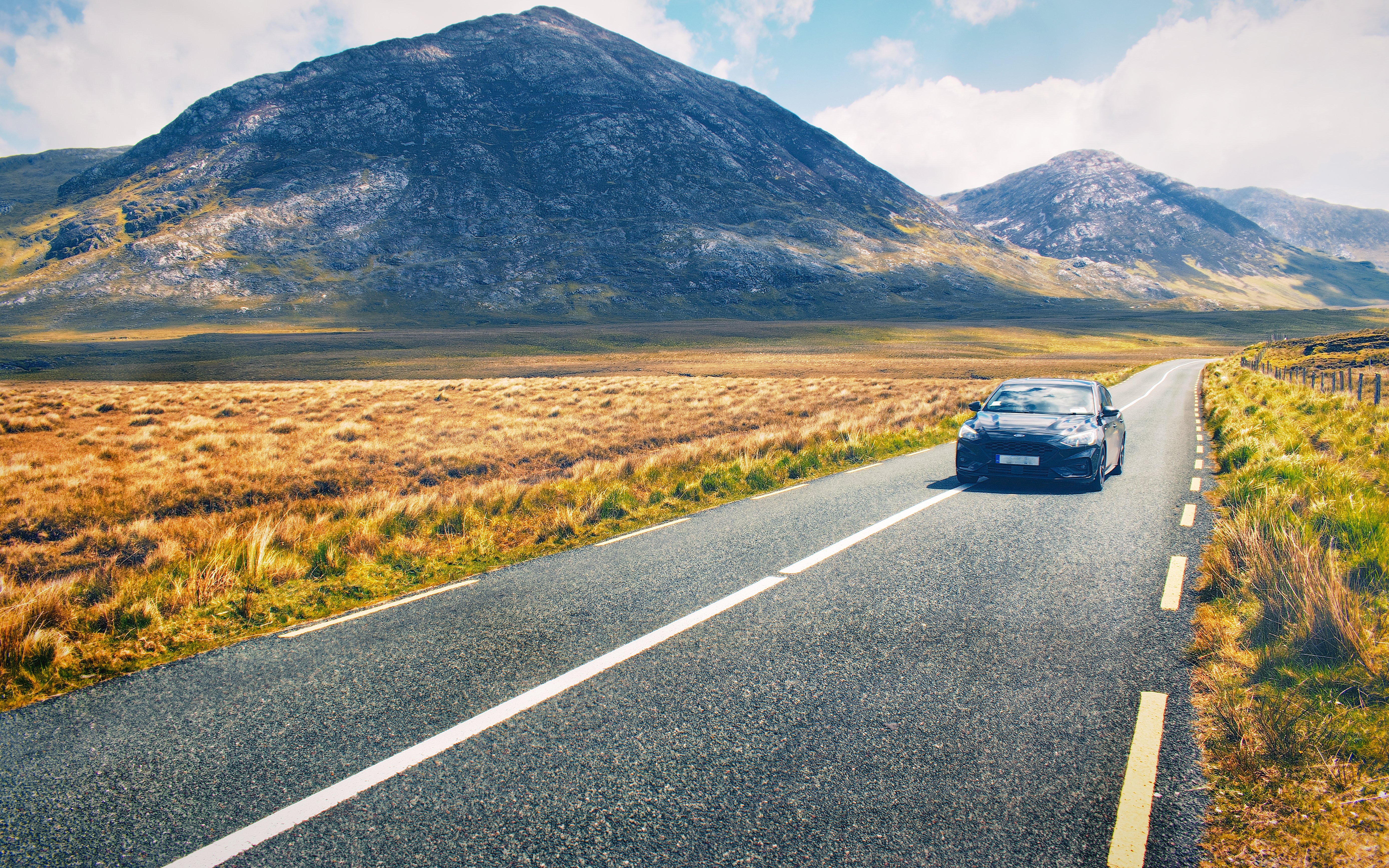Car driving on a scenic road through the Irish countryside with mountains in the background.