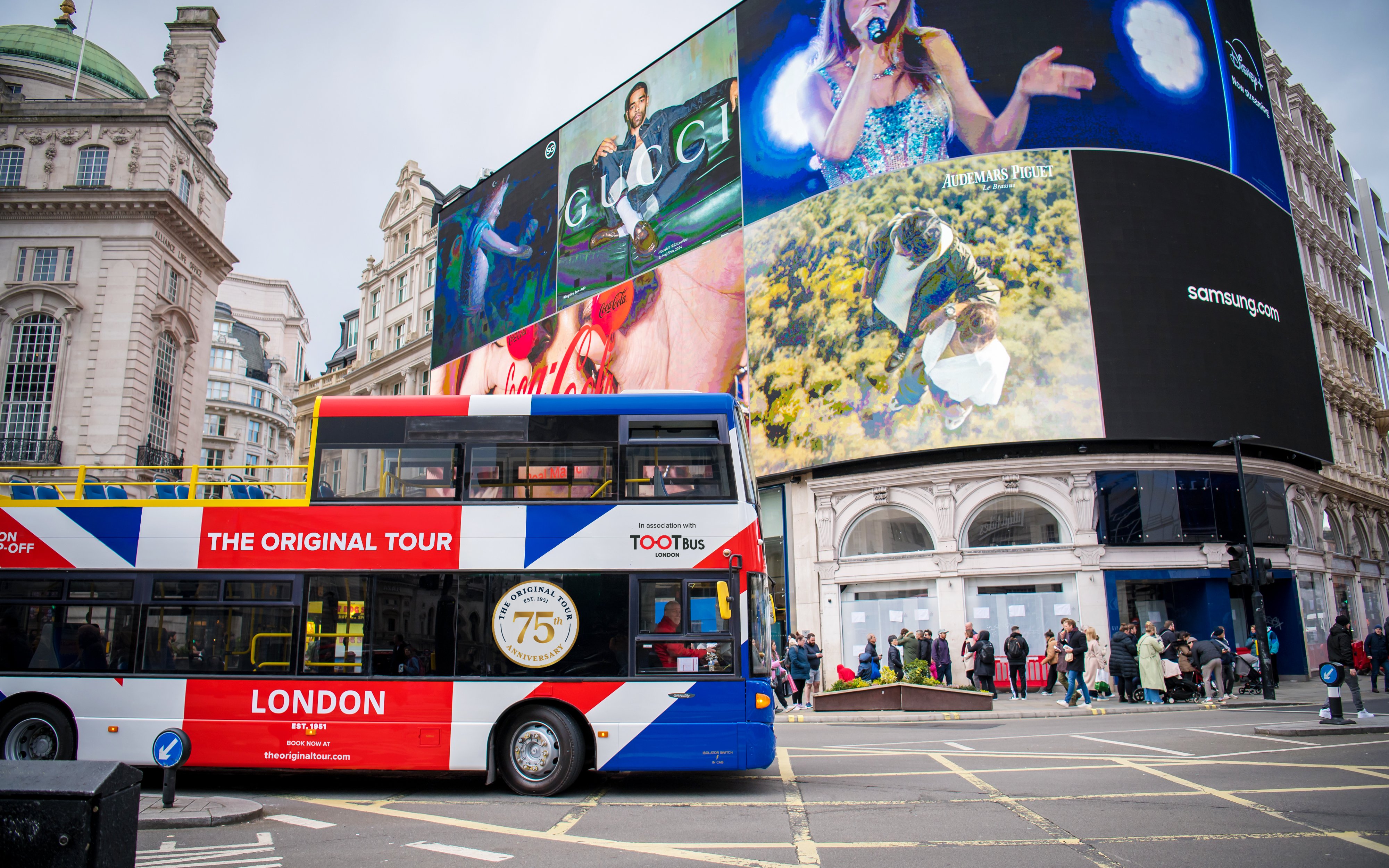 Tootbus passing through Piccadilly Circus in London with iconic digital billboards.