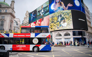 Tootbus passing through Piccadilly Circus in London with iconic digital billboards.