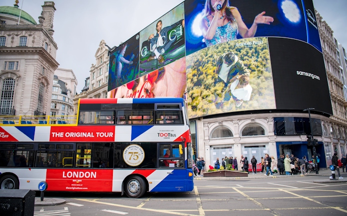 Tootbus passing through Piccadilly Circus in London with iconic digital billboards.