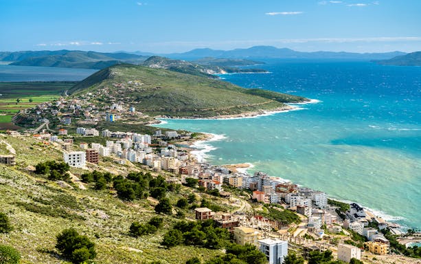 Aerial view of Saranda city coastline with buildings and lush hills, Albania.