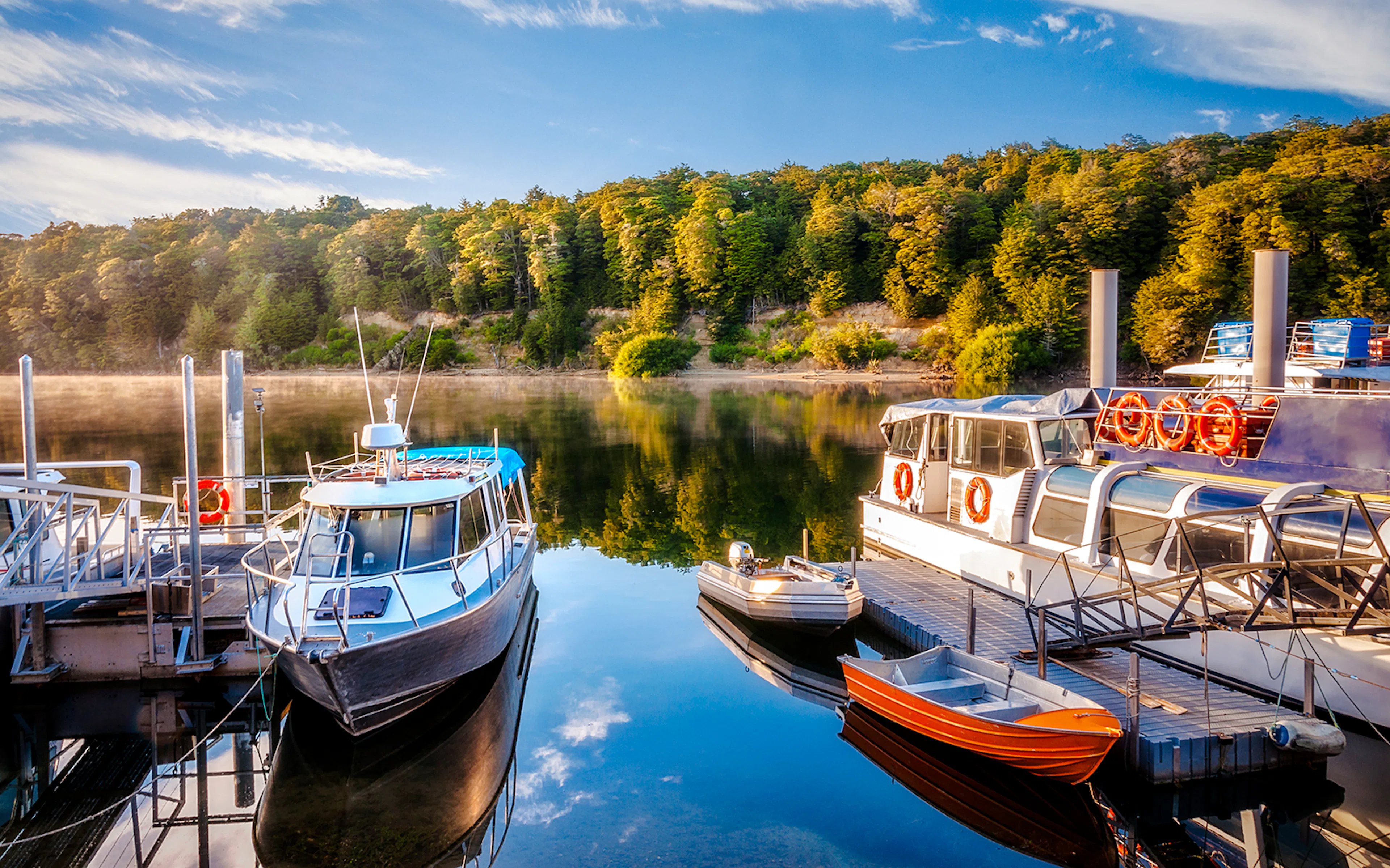 Boats docked at Lake Manapouri harbour with forested hills in the background.