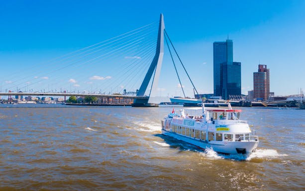Rotterdam river cruise boat passing under Erasmus Bridge with city skyline in the background.