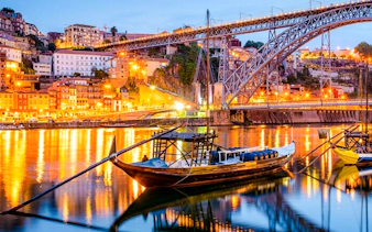 Dom Luís I Bridge over Douro River at sunset in Porto, Portugal with traditional boats.