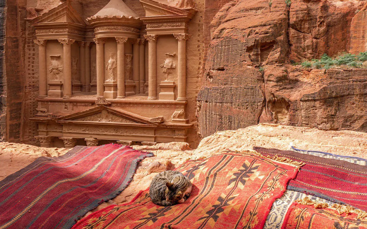Petra's Treasury with colorful rugs and a resting cat in Jordan.