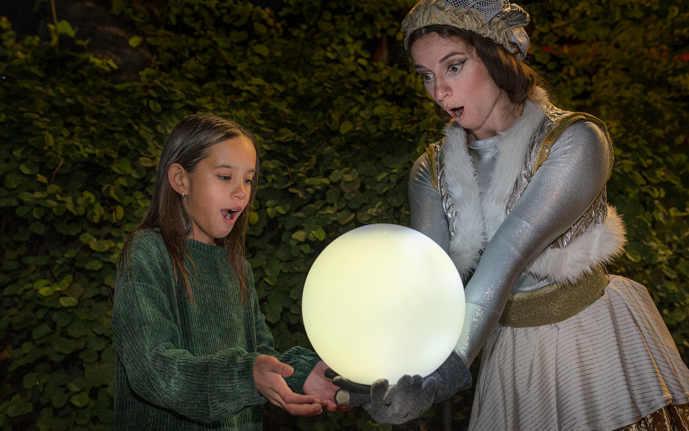 Child and performer holding glowing orb at San Diego Zoo Aurora event.