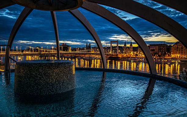 Rudas Baths rooftop pool with city lights and river view, Budapest, New Year’s Eve party setting.