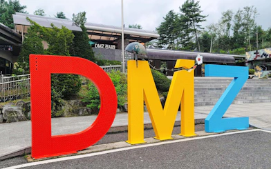 DMZ sign at entrance of exhibition hall in Korea, surrounded by trees and steps.