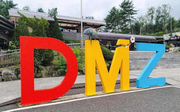 DMZ sign at entrance of exhibition hall in Korea, surrounded by trees and steps.