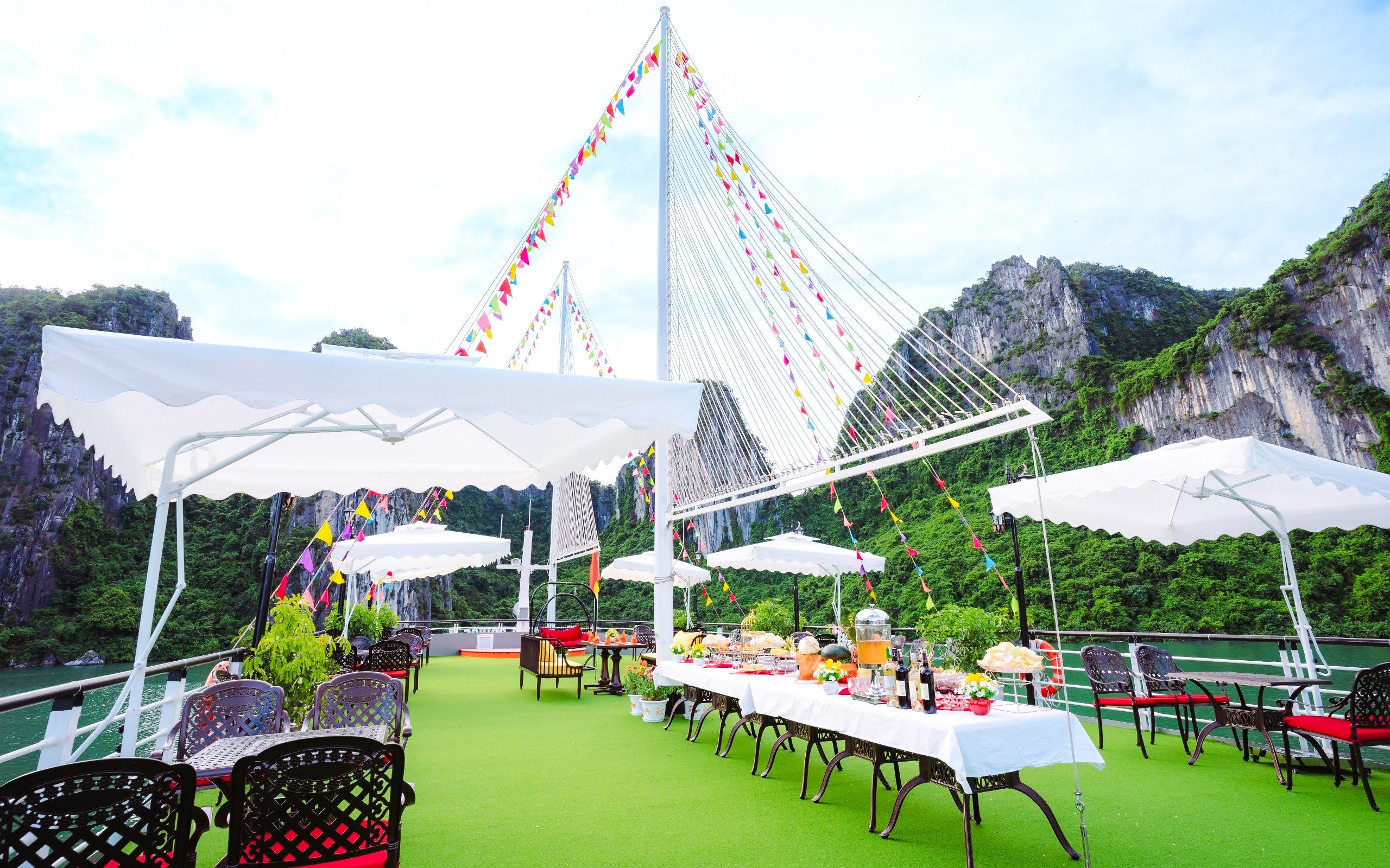 Deck of Apollo Cruise with dining setup, Ha Long Bay, limestone cliffs in background.
