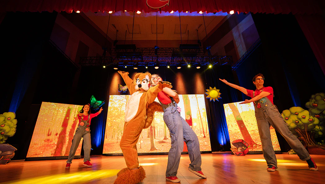 Performers in colorful costumes on stage during Cantajuegos 20 Años show.