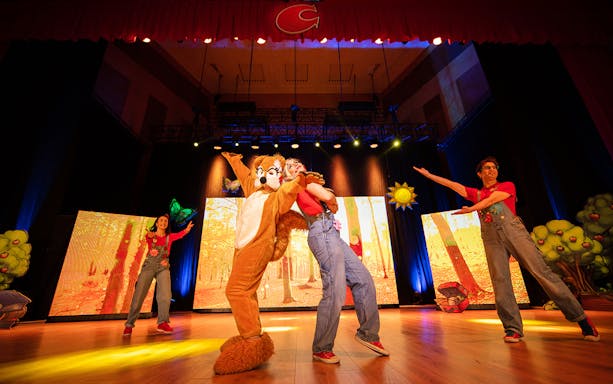 Performers in colorful costumes on stage during Cantajuegos 20 Años show.