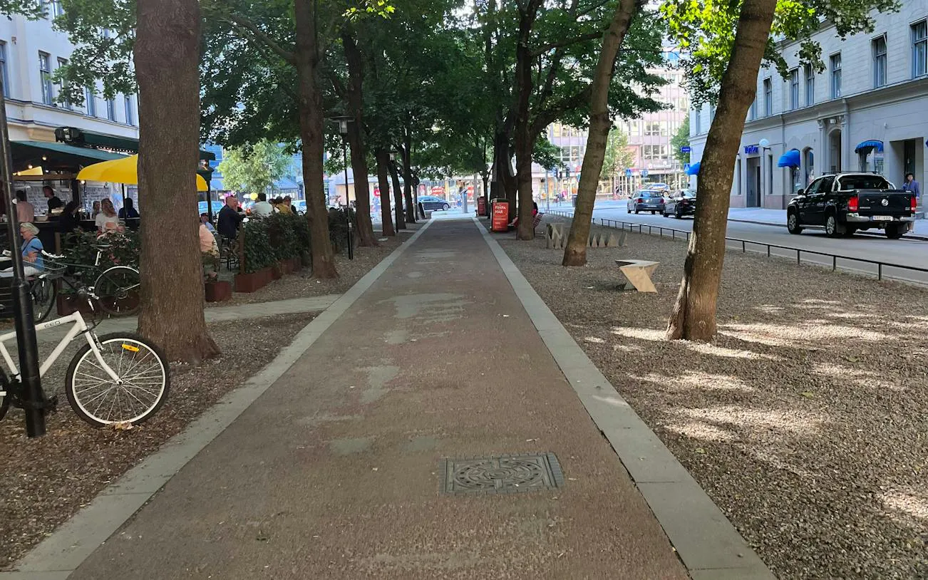 Tree-lined path in Södermalm, Stockholm, with outdoor café seating and parked bicycles.