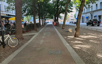 Tree-lined path in Södermalm, Stockholm, with outdoor café seating and parked bicycles.
