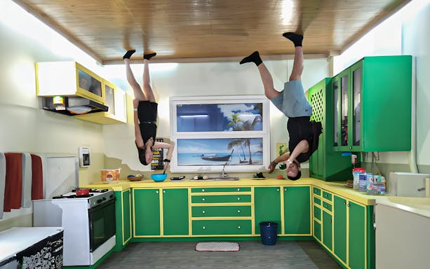 Visitors standing upside down in a kitchen at Upside Down World Bali.