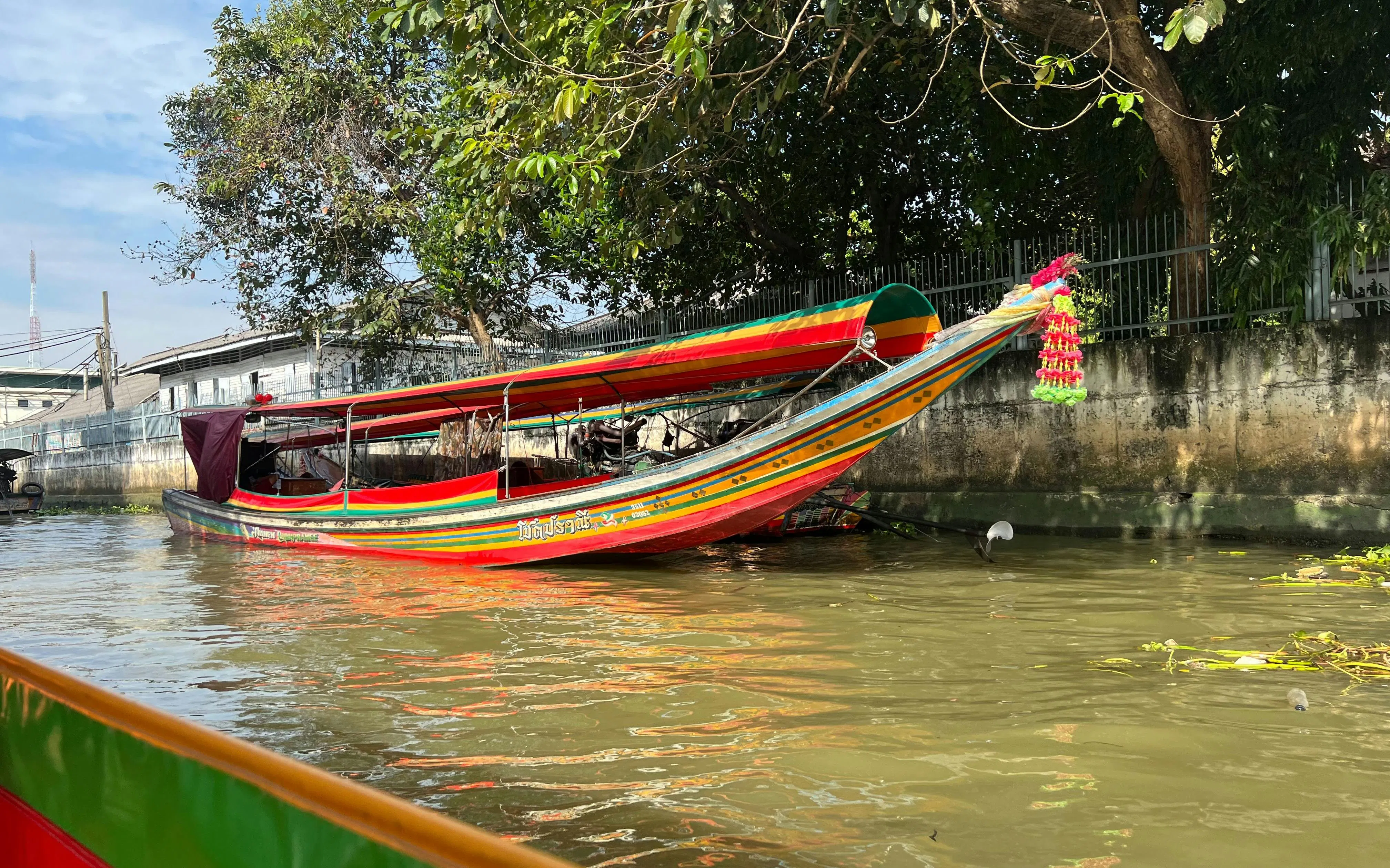 Longtail boat on Bangkok canal with colorful decorations and trees in the background.