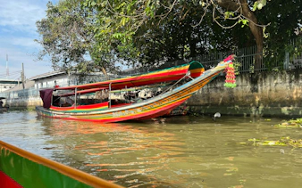 Longtail boat on Bangkok canal with colorful decorations and trees in the background.