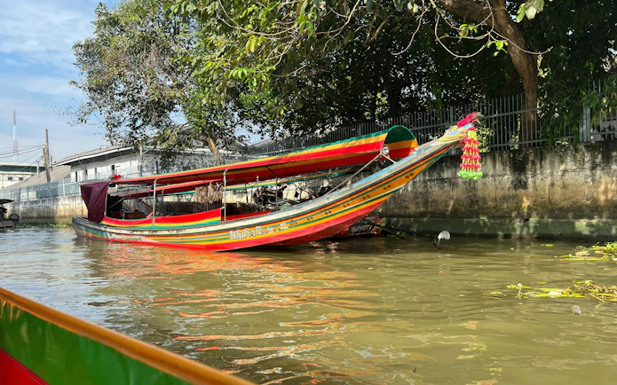 Longtail boat on Bangkok canal with colorful decorations and trees in the background.