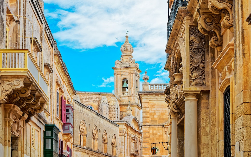Historic architecture in Mdina, Malta with ornate stone carvings and a bell tower.
