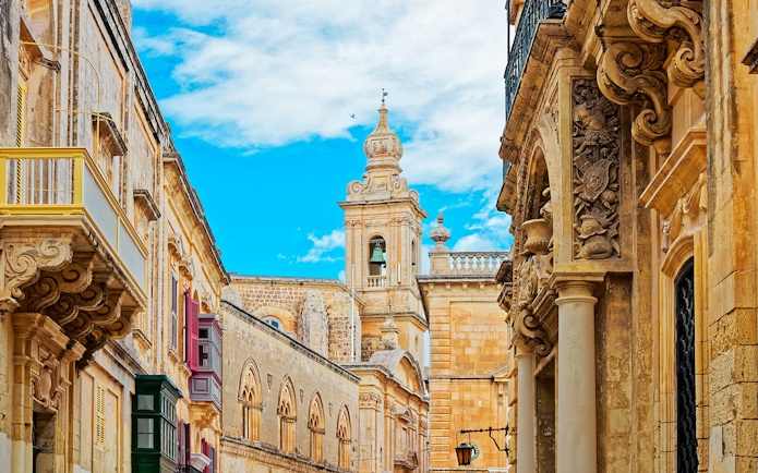 Historic architecture in Mdina, Malta with ornate stone carvings and a bell tower.