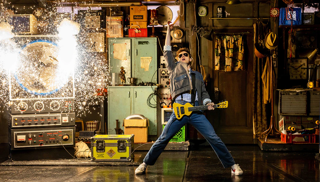 Man in denim jacket with guitar in a workshop, sparks flying from a machine, Back to the Future theme.