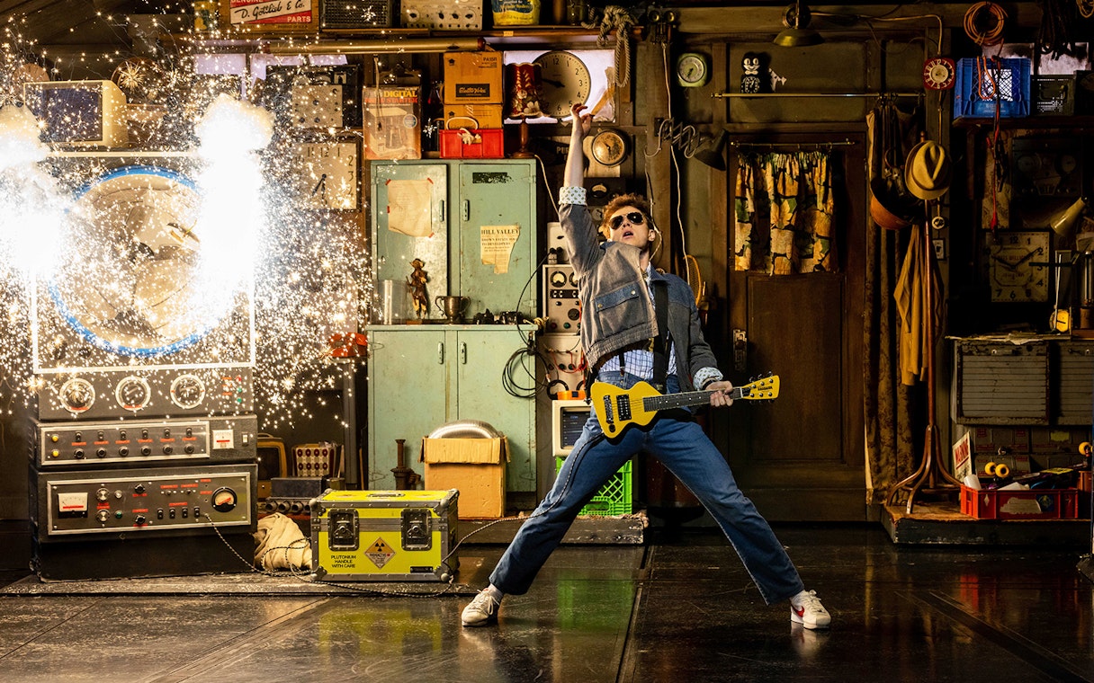Man in denim jacket with guitar in a workshop, sparks flying from a machine, Back to the Future theme.