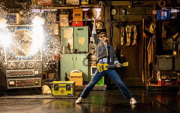 Man in denim jacket with guitar in a workshop, sparks flying from a machine, Back to the Future theme.