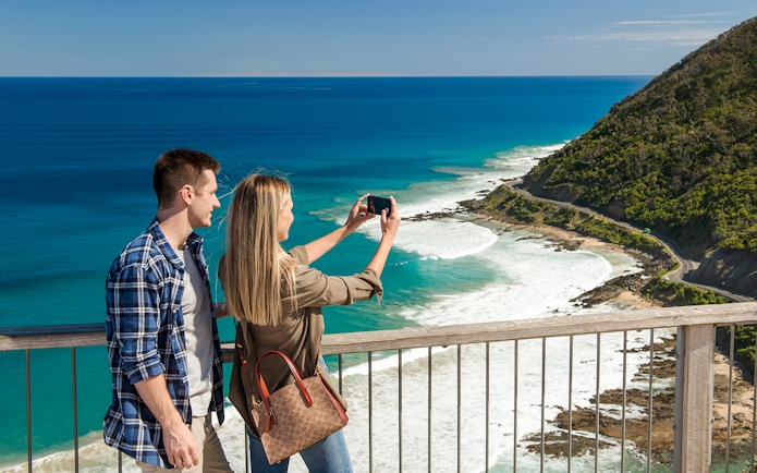 Couple taking a photo at Teddy's Lookout with a view of the Great Ocean Road coastline.