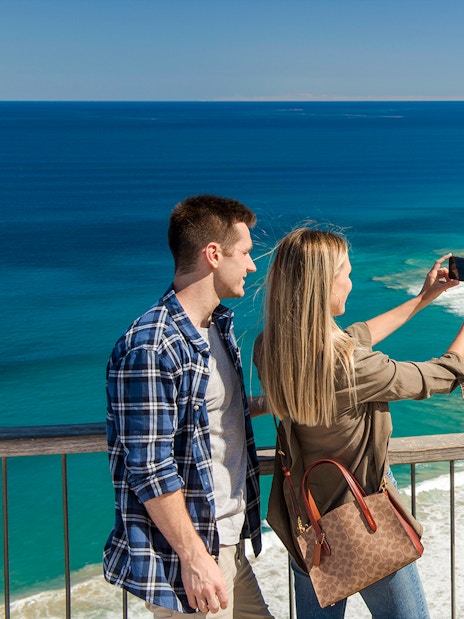 Couple taking a photo at Teddy's Lookout with a view of the Great Ocean Road coastline.