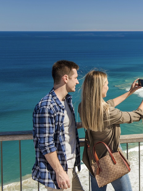 Couple taking a photo at Teddy's Lookout with a view of the Great Ocean Road coastline.
