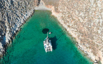 Catamaran anchored in clear waters near rocky Heraklion coastline.