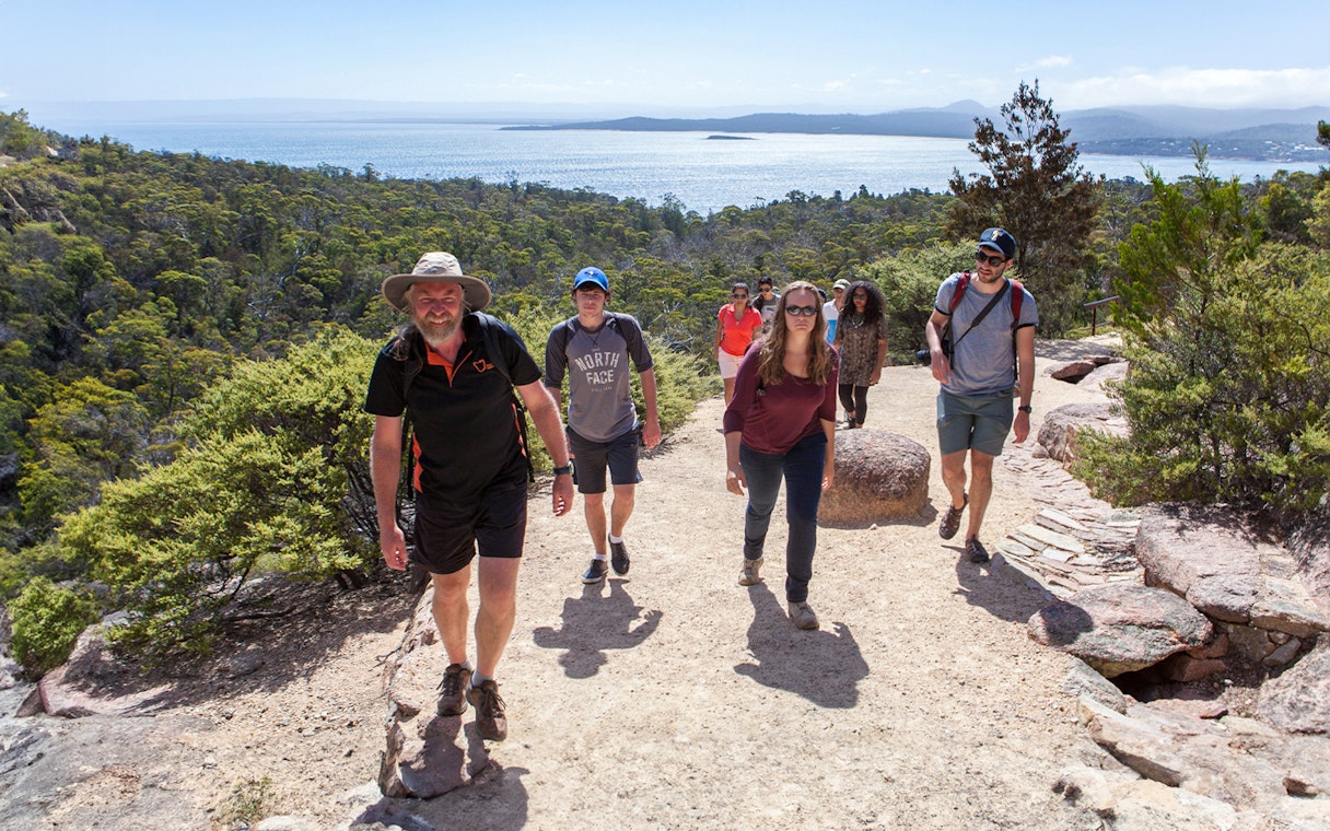 Group hiking on a trail with views of Wineglass Bay, Tasmania.