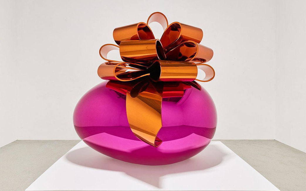 Sculpture of a large pink metallic egg with an orange bow at Moco Museum London exhibit.