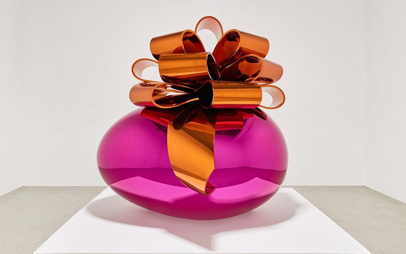 Sculpture of a large pink metallic egg with an orange bow at Moco Museum London exhibit.