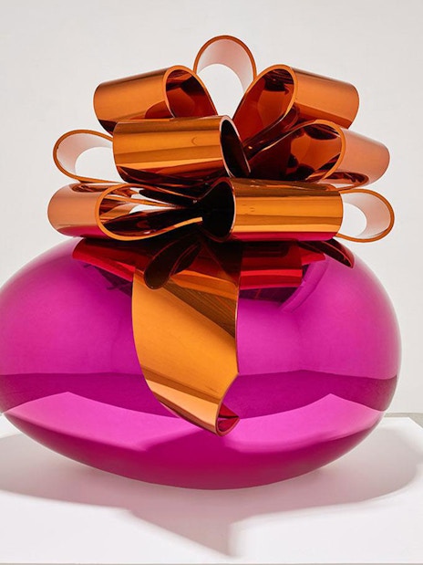 Sculpture of a large pink metallic egg with an orange bow at Moco Museum London exhibit.