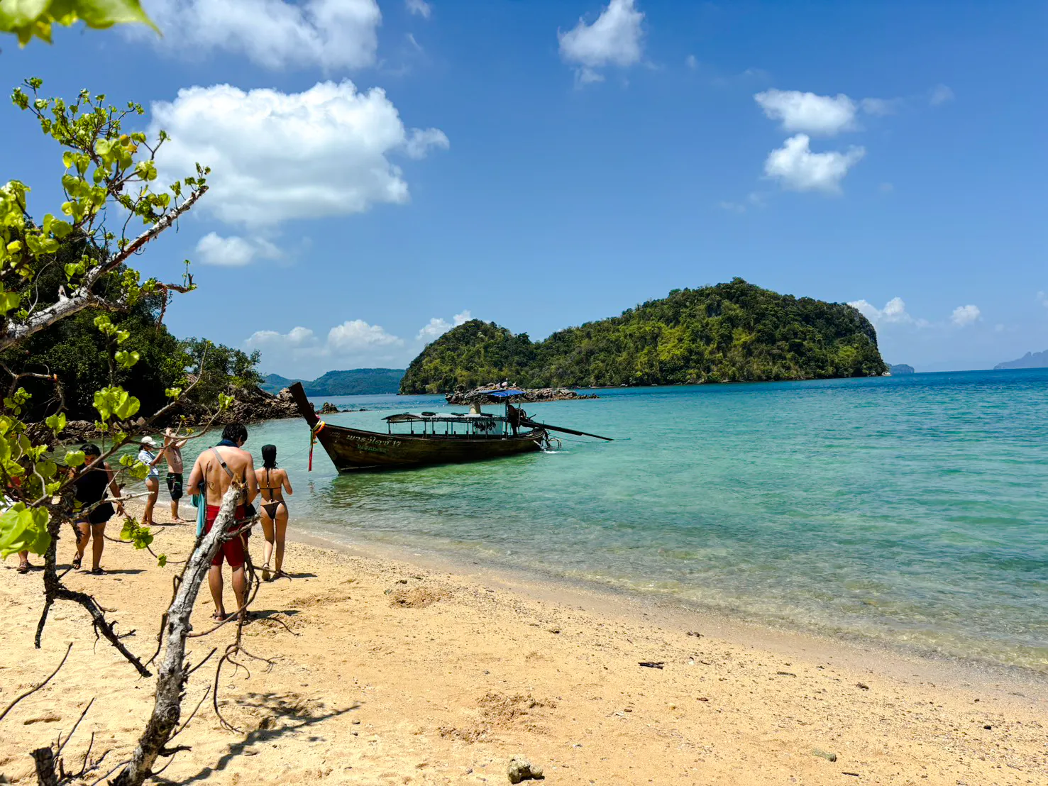 Tourists walking on a sandy beach towards a longtail boat in Krabi, with Hong Islands in the background.