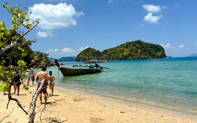 Tourists walking on a sandy beach towards a longtail boat in Krabi, with Hong Islands in the background.
