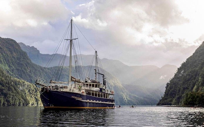 Cruise ship on Doubtful Sound surrounded by lush mountains, Te Anau.