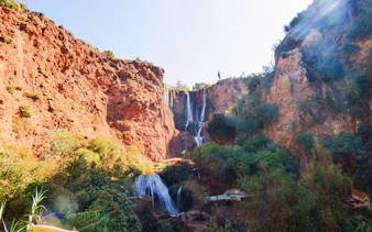 Ouzoud Waterfalls cascading down red cliffs surrounded by lush greenery in Morocco.